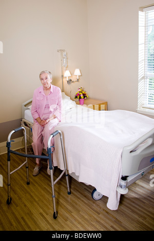 Ältere Frau sitzt am Krankenhausbett mit walker Stockfoto