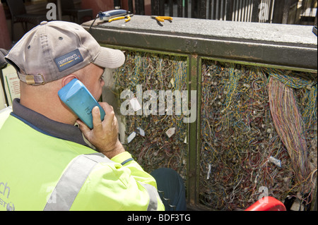 Blick über die Schulter des BT Nachrichtentechniker am Telefon vor der offenen Verdrahtung Anschlussdose auf Straße Stockfoto