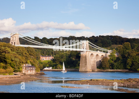 Yachtcharter Segeln unter Menai Suspension Bridge von Thomas Telford über Menaistraße vom Festland gebaut. Menai Bridge, von der Insel Anglesey, Nordwales, Großbritannien Stockfoto