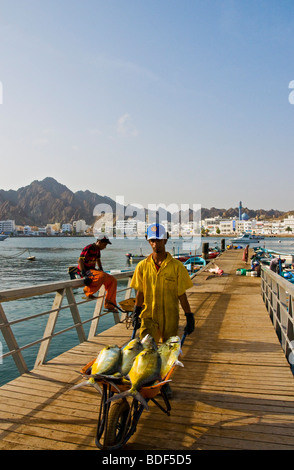 Fischer am Mutrah Fischmarkt docks mit alten Muscat im Hintergrund Stockfoto