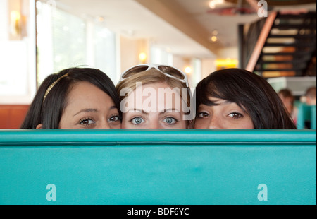 Drei Mädchen im Teenageralter Blick hinter einen Stuhl Stockfoto