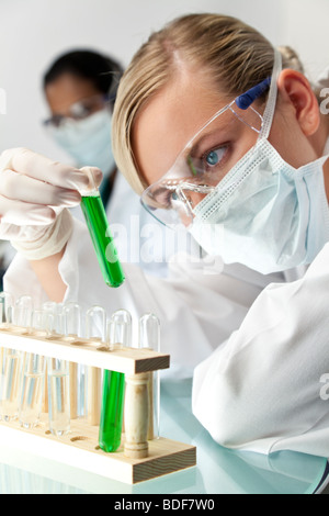 Eine blonde medizinische oder wissenschaftliche Forscher oder Arzt mit Blick auf eine grüne Lösung in einem Labor Stockfoto