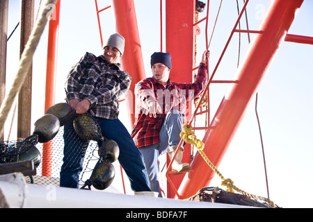 Junge Fischer in karierten Hemden ziehen Netze am Fischerboot Stockfoto
