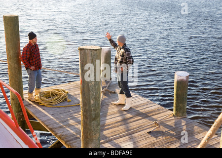 Junge Fischer in karierten Hemden stehen am Pier mit einem Seil in der Nähe von Fischerboot Stockfoto
