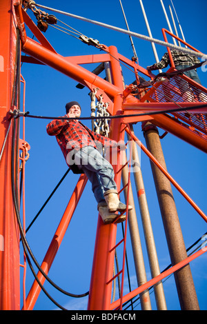 Junge Fischer im karierten Hemd Klettern auf Fischerboot und Daumen aufgeben Stockfoto