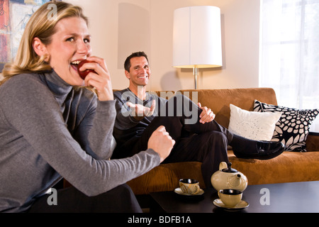 Glückliches Paar im Wohnzimmer, Frau einen Apfel beißen Stockfoto