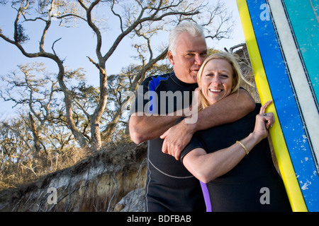 Paar mittleren Alters in Neoprenanzüge holding Surfbrett am Strand Stockfoto