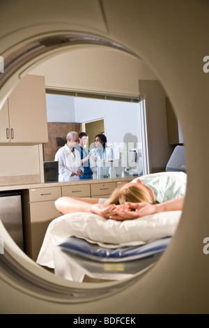 Patienten, die auf CAT-Scan-Maschine liegend, während im Hintergrund Ärzte konsultieren Stockfoto