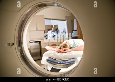 Patienten, die auf CAT-Scan-Maschine liegend, während im Hintergrund Ärzte konsultieren Stockfoto