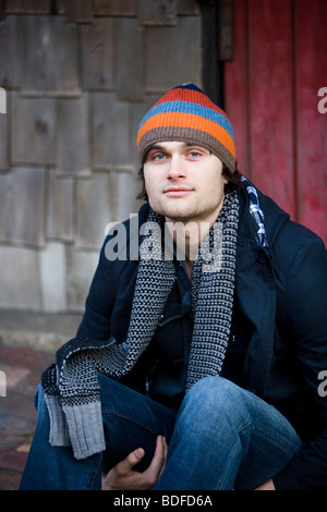 Porträt des jungen Mannes tragen warme Kleidung draußen sitzen hautnah Stockfoto