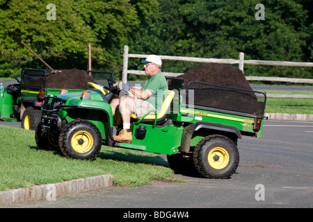 Ein Gärtner mit einer Belastung von Mulch im Bett von einem John Deere Nutzfahrzeug zu vertreiben. Stockfoto