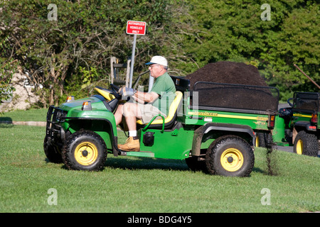 Ein Gärtner mit einer Belastung von Mulch im Bett von einem John Deere Nutzfahrzeug zu vertreiben. Stockfoto