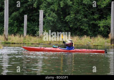 rote Kajak auf ruhigem grünen Wasser gelbe Paddel grünen Bäumen Küste Rasen im Hintergrund Stockfoto