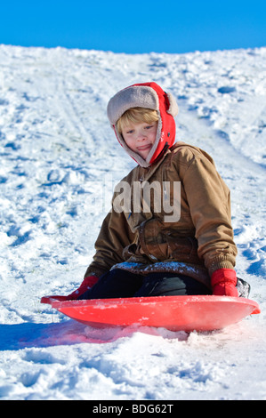 Ein Junge Schlitten hinunter einen verschneiten Hang unter einem strahlend blauen Wisconsin Winterhimmel. Stockfoto