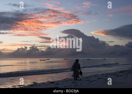 Die einsame Gestalt einer Frau in der Dämmerung. Sonnenaufgang über dem Meer, an der Küste in Paje Beach, Zanzibar. Stockfoto