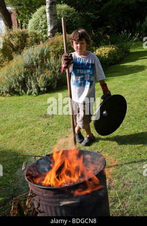 Jungen im Alter von sieben brennende Gartenabfälle im Verbrennungsofen mit Rauch und Flammen. Stockfoto