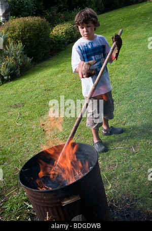 Jungen im Alter von sieben brennende Gartenabfälle im Verbrennungsofen. Stockfoto
