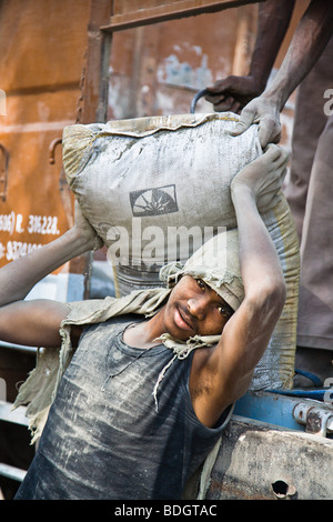 Ein junger Mann entlädt Zement-Taschen aus einem LKW. Foto in Gujarat, Indien auf einer Baustelle Stockfoto