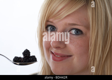 junge 20 jährige blonde Frau mit einem Löffel frische Brombeeren mit einem glücklich lächelnden Gesicht Stockfoto