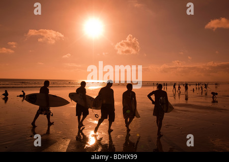 Indonesien, Bali, Kuta, Strand, Gruppe von männlichen Surfer bei Sonnenuntergang entlang nassen Sand am Ende der Tage Surfen Stockfoto