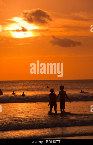 Indonesien, Bali, Kuta, Strand, paar im seichten Wasser bei Sonnenuntergang Stockfoto