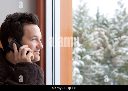 Mann im Bademantel am Handy sprechen und schaut aus dem Fenster Stockfoto