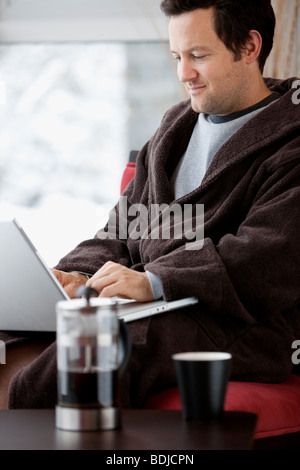 Mann im Bademantel mit Laptop-Computer Stockfoto