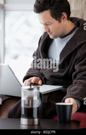 Mann im Bademantel mit Laptop-Computer und eine Tasse Kaffee trinken Stockfoto