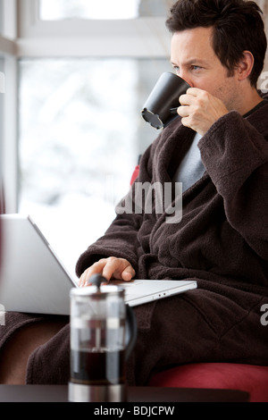 Mann im Bademantel mit Laptop-Computer und eine Tasse Kaffee trinken Stockfoto