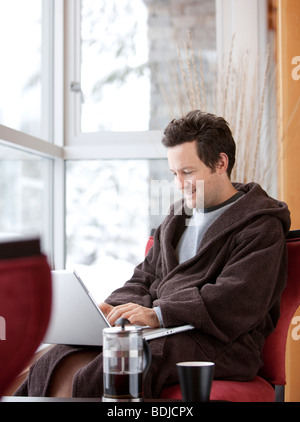 Mann im Bademantel mit Laptop-Computer Stockfoto