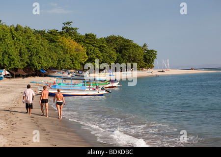 Indonesien, Lombok, Sengiggi, paar walking bunte Ausleger Angelboote/Fischerboote am Strand Stockfoto