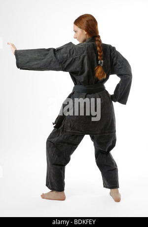 Mädchen in schwarzen uniform steht wieder auf Hälfte gebogenen Beinen, linke Hand hob behindern, isoliert auf weiss Stockfoto