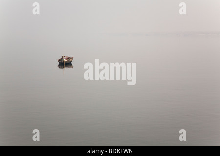 Ein Fährmann nimmt eine Auszeit in seinem Holzboot am Fluss Ganga (Ganges) in Varanasi, Indien. Stockfoto