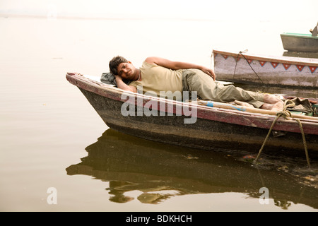 Ein Fährmann nimmt eine Pause in seinem Ruderboot festgemacht an den Ufern des Flusses Ganga (Ganges) in Varanasi, Indien. Stockfoto