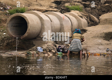 Ein Dhobi (Wäsche Mann) wäscht Kleidung neben einem plätschernden Abfluss an den Ufern des Flusses Ganga (Ganges) in Varanasi, Indien. Stockfoto