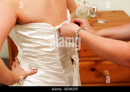 Braut in Brautkleid am Tag der Hochzeit hinten gebunden Kleid geschnürt geholfen zugeknöpft festen moderne Hochzeitsfotografie Stockfoto