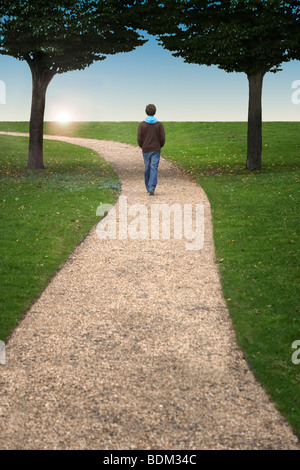 Ein Junge auf einem gewundenen Pfad zwischen zwei Bäumen in Richtung einer untergehenden Sonne Wandern Stockfoto