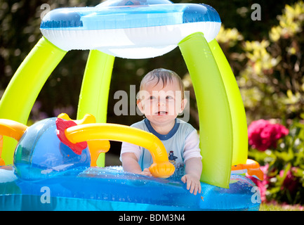 Einen kleinen Jungen an einem Sommertag in einem aufgeblasenen Kunststoff Boot Planschbecken spielen. Stockfoto
