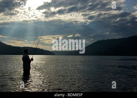 Mann in Silhouette Spin Casting Köder beim Strand Angeln für Buckellachs Stockfoto