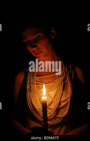Mädchen mit brennender Kerze und Perlenkette im Dunkeln Stockfoto