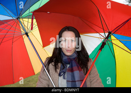 Junge Frau, 30-35 Jahre, schützen sich mit zwei bunten Sonnenschirmen gegen dem kalten Winterwetter Stockfoto