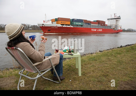 Junge Frau, 30-35 Jahre frühstücken an einem feuchten Wintertag am Nord-Ostsee-Kanal, gerade vorbeifahrenden Schiffen, Schleswig-Holstein, Stockfoto