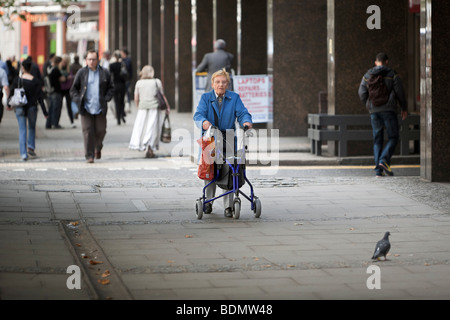 Eine teilweise behinderte ältere Frau mit einem fahrbaren Rahmen Wandern in central London, UK Stockfoto
