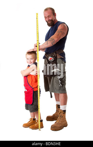 Vater tragen Werkzeuggürtel mit Spielzeug Hammer und Bandmaß, misst die Höhe des niedlichen Sohn gekleidet in orange Schürze, isoliert. Stockfoto