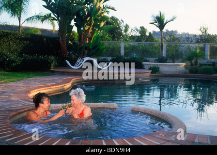 Oma mit Schwiegertochter Toasten das gute Leben im Garten Whirlpool zu Hause in Südkalifornien Stockfoto