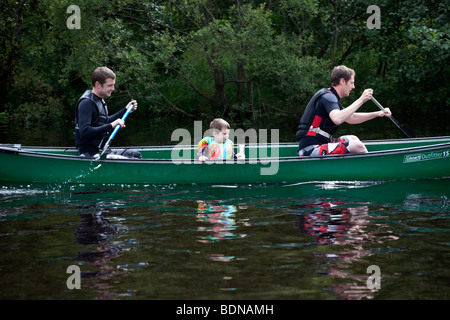 Zwei Männer und ein Junge in einem grünen Kanu an einem Fluss zu Loch Lomond, Schottland. Stockfoto