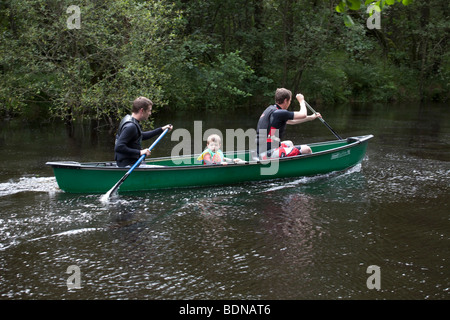 Zwei Männer und ein Junge in einem grünen Kanu an einem Fluss zu Loch Lomond, Schottland. Stockfoto