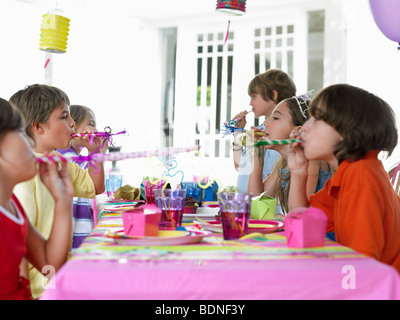 Sechs Kinder (7-12 Jahre) am Tisch, weht Partei Kugelfische, Seitenansicht Stockfoto