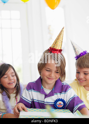 Drei Kinder (7-12 Jahre) Geburtstag feiern, ein Junge öffnen vorhanden Stockfoto