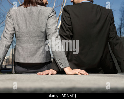 Business-Mann und Frau sitzen an Wand im Freien, Rückansicht (beschnitten) Stockfoto